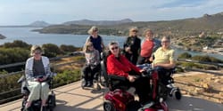 John pictured with six Wheelchair Travel readers, all women, in front of the Greek coastline.
